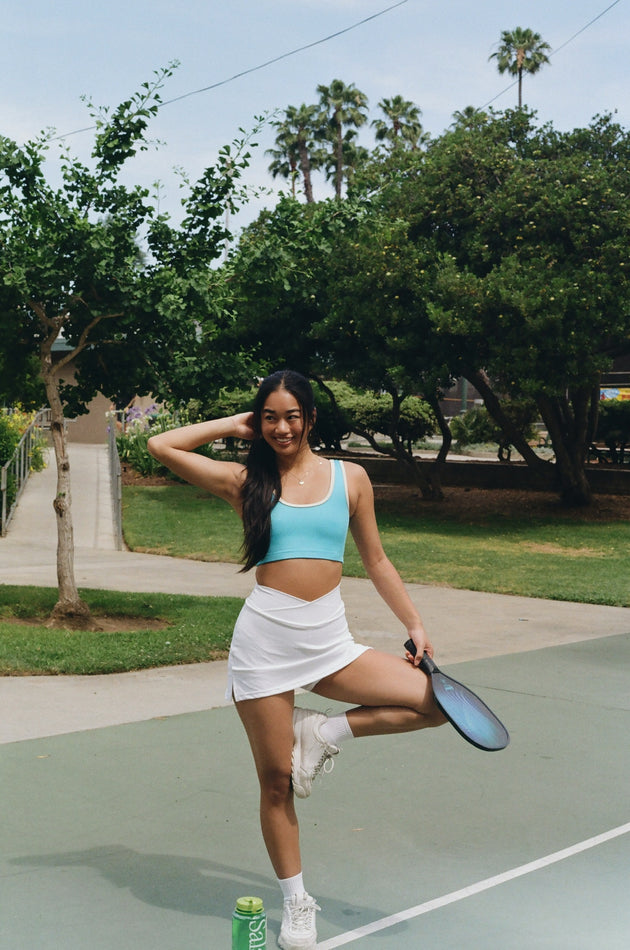 Woman on a tennis court holding a paddle with trees and grass in the background