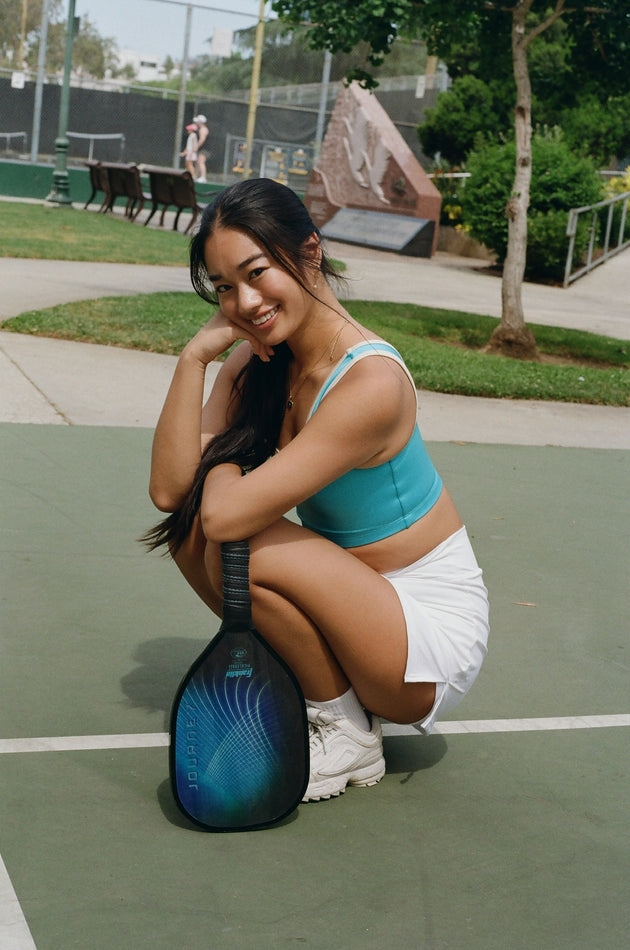 Woman posing with a pickleball paddle on a court
